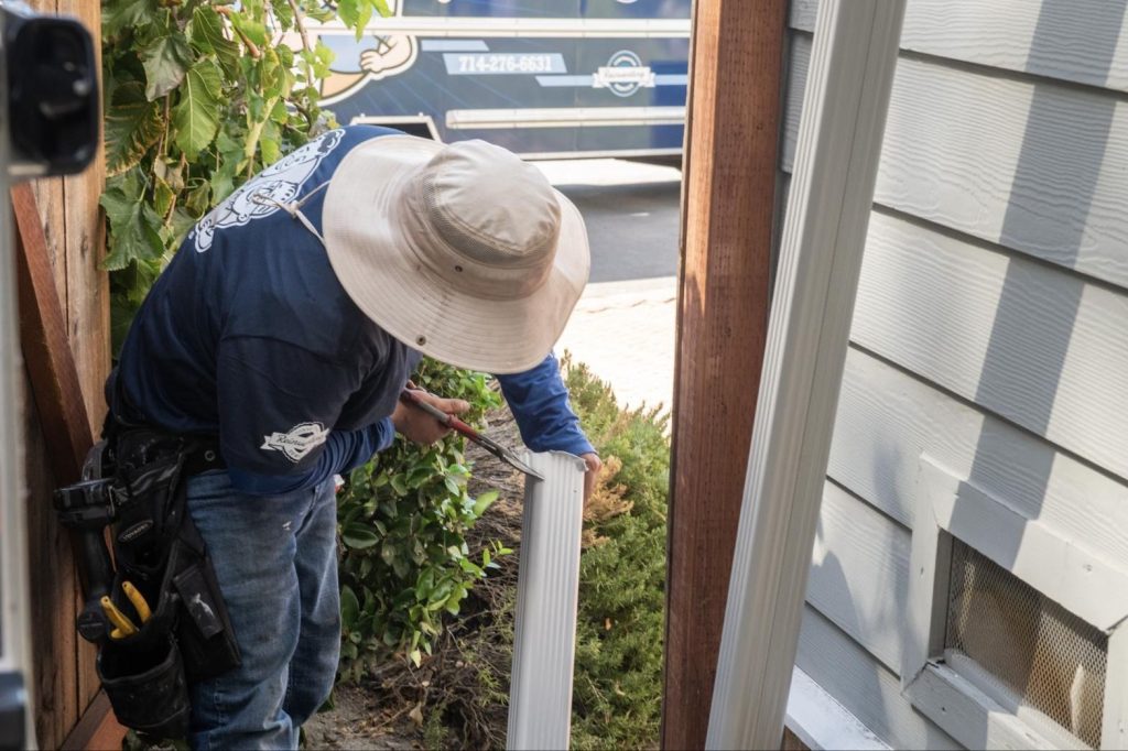 Installer cutting a downspout to length beside the house